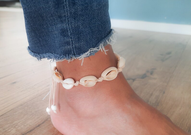 May include: A white seashell anklet with a white string and white beads. The anklet is on a person's ankle.