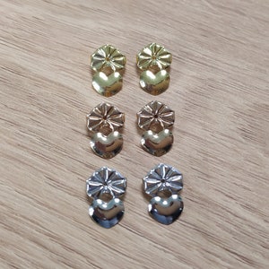 Pode incluir: Seis pares de fechos para brincos, tr&ecirc;s pares s&atilde;o dourados e tr&ecirc;s pares s&atilde;o prateados. Cada par tem uma pe&ccedil;a em forma de cora&ccedil;&atilde;o e uma pe&ccedil;a redonda com um desenho de flor.