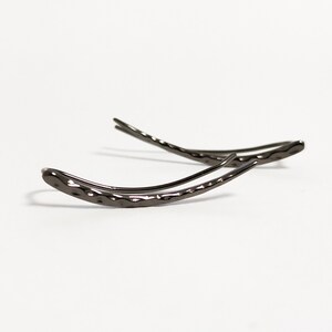 May include: A pair of dark gray ear climbers with a hammered texture. The earrings curve upwards, with a sleek, modern design. The jewelry is set against a white background.