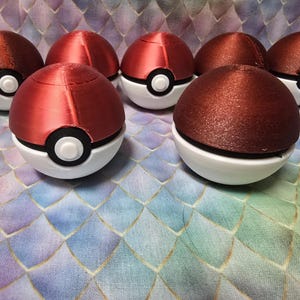 May include: Seven red and white Poké Ball replicas with black and white accents. The top halves are a glossy red, while the bottoms are white. The balls are arranged on a patterned, multi-colored surface.