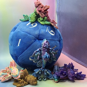 May include: A blue plush dice with the numbers 1, 6, and 19 visible.  The dice is surrounded by colorful, 3D printed, winged creatures with intricate details.