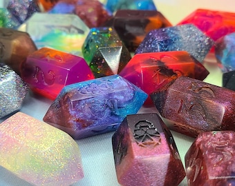May include: A close-up of a collection of colorful, iridescent dice with various symbols and designs. The dice are made of resin and have a glittery finish.