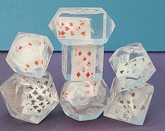 Puede incluir: Seis dados de resina transparente con diseños de cartas de juego incrustados. Los dados están numerados del 1 al 6 y presentan diferentes palos de cartas, incluyendo corazones, diamantes, tréboles y picas.