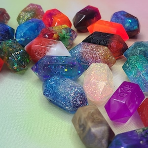 May include: A collection of 20-sided dice with various colors and glitter accents. The dice are made of clear resin and have a variety of colors, including red, blue, green, purple, and white. The dice are all in focus and are arranged in a random pattern.
