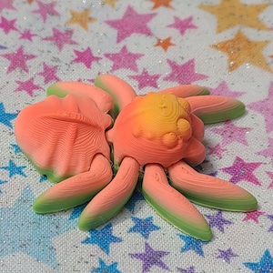 Puede incluir: Un juguete de araña impreso en 3D con un degradado de color rosa brillante, naranja y verde. La araña tiene ocho patas y un cuerpo redondo.