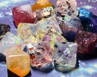May include: A collection of 10 colorful dice with various patterns and glitter embedded in the clear resin. The dice are in a variety of colors, including pink, purple, blue, green, and yellow.