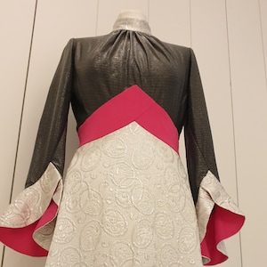 Peut inclure: Une robe à manches longues avec un col montant et une jupe à motifs argentés et blancs. Le haut de la robe est noir avec une bande rose sur la poitrine.