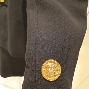 May include: A black blazer with a gold button featuring a crest design.