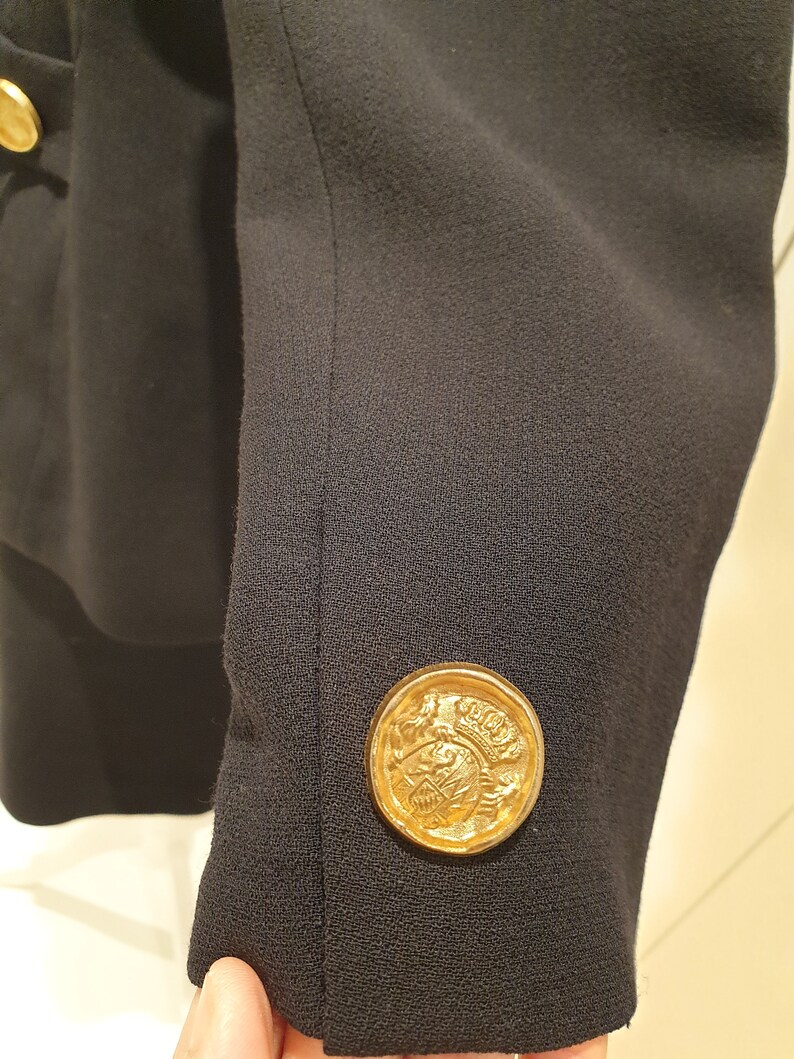 May include: A black blazer with a gold button featuring a crest design.