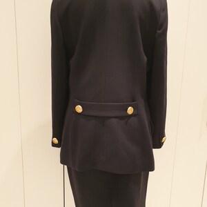 May include: A black blazer and skirt suit with gold buttons. The blazer has long sleeves and a double-breasted closure. The skirt is knee-length and has a straight silhouette.