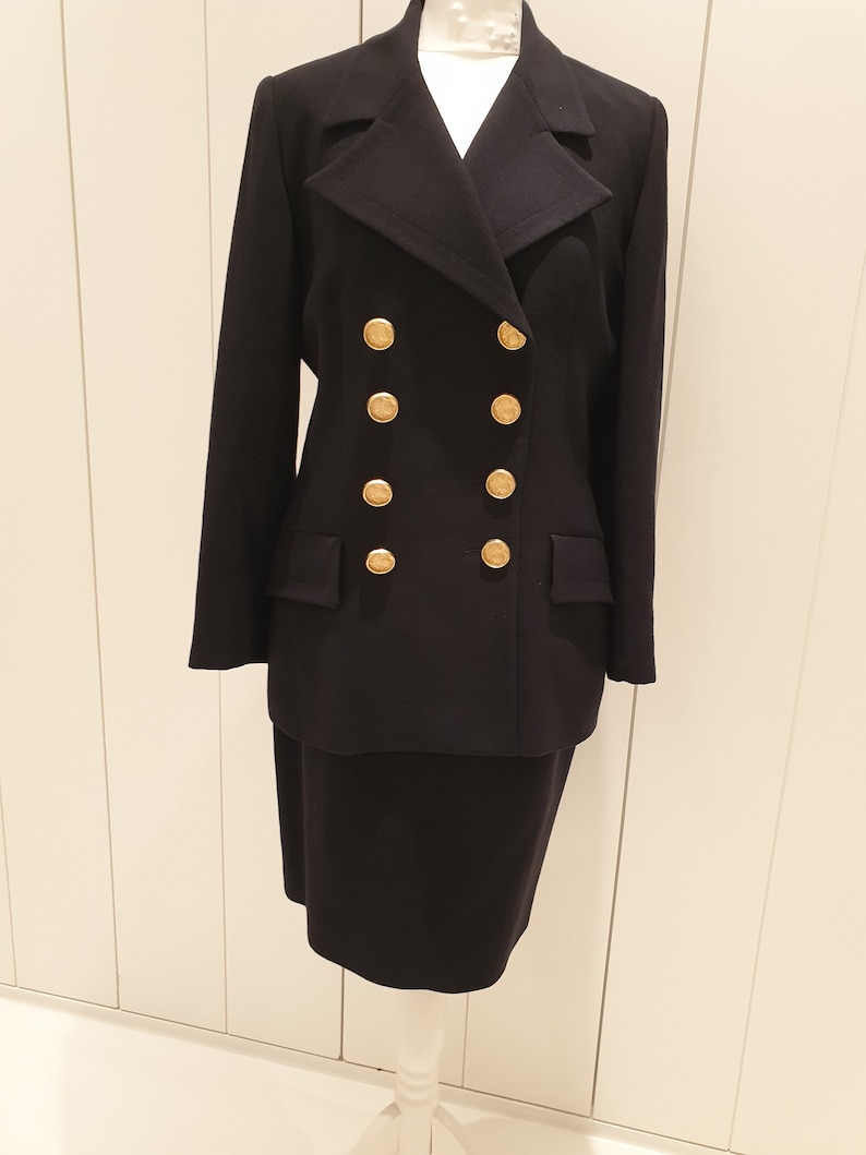 May include: A black double-breasted blazer with gold buttons and a matching skirt. The blazer has a notched collar and long sleeves.
