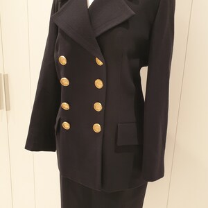 May include: A black double-breasted blazer with gold buttons and a matching skirt. The blazer has a classic collar and long sleeves. The skirt is knee-length and has a straight silhouette.