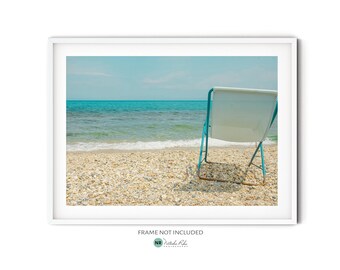 May include: A blue beach chair sits on a sandy beach with turquoise water in the background.