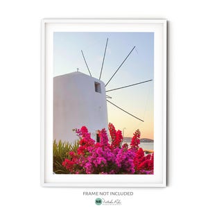 Könnte beinhalten: Eine weiße Windmühle mit einem Holzrahmen vor blauem Himmel. Im Vordergrund befinden sich rosa Blüten.