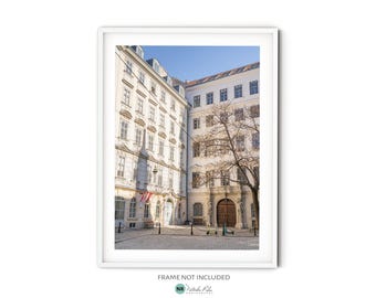 May include: A photograph of a courtyard in Vienna, Austria. The courtyard is surrounded by tall, white buildings with windows. A tree with bare branches stands in the center of the courtyard. The buildings have a classic European architectural style.
