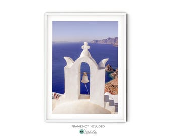 May include: A white bell tower with a bell inside, overlooking a blue ocean and a rocky coastline. The tower is decorated with white arches and a cross on top.