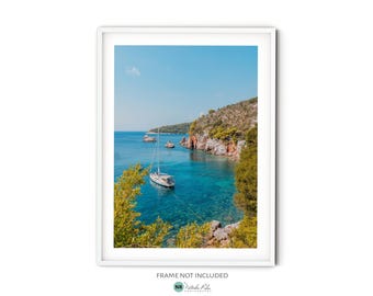 May include: A sailboat anchored in a turquoise cove surrounded by lush green hills. The water is crystal clear and the sky is a bright blue.