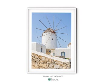 May include: A white windmill with a thatched roof stands against a bright blue sky. The windmill is surrounded by whitewashed buildings and a stone wall.