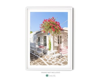May include: A white building with a pink door and pink steps. There are white tables and chairs outside the building. A pink bougainvillea bush is in front of the building.