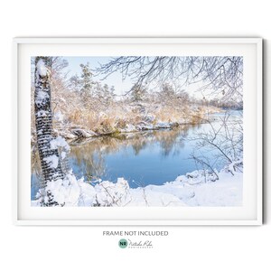Può includere: Una scena invernale innevata con un lago ghiacciato e alberi coperti di neve. Il lago riflette il cielo blu e gli alberi proiettano ombre sulla neve.