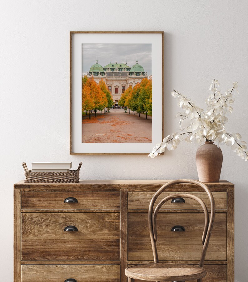 May include: A framed photograph of a white building with green domes and a pathway lined with trees in autumn. The trees have orange leaves and the ground is covered in fallen leaves.