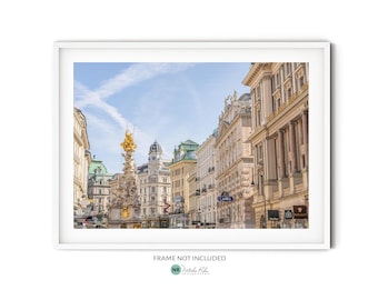 May include: A photograph of a street in Vienna, Austria. The street is lined with tall buildings, some of which have ornate facades. In the center of the image is a large, golden statue. The sky is blue and there are clouds in the distance.