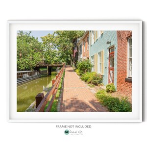 Puede incluir: Un camino de adoquines bordeado de casas coloridas conduce a un canal con un barco atracado en el agua. Las casas tienen una mezcla de pintura azul, verde y roja. Una exuberante vegetación rodea el camino y el canal.