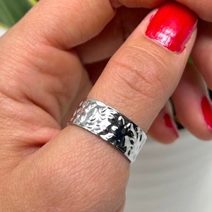 Könnte beinhalten: Ein silberner, gehämmerter Daumenring. Der Ring wird am Daumen einer Person getragen. Die Fingernägel der Person sind rot lackiert.