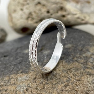 Op de afbeelding: Een zilveren teenring met een delicaat, getextureerd ontwerp. De ring is open en verstelbaar.