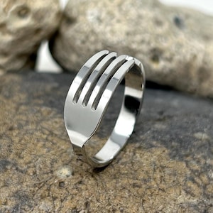 May include: A silver ring with a fork design. The ring is sitting on a pile of rocks.