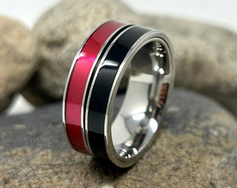 May include: A silver ring with a black and red inlay. The ring is sitting on a pile of rocks.