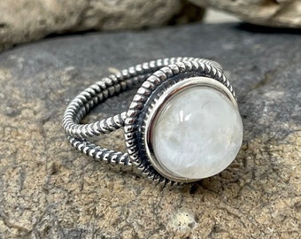 May include: A silver ring with a white moonstone set in a twisted band.
