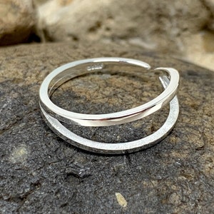 May include: A silver ring with a double band design. The ring is made of two bands that are intertwined and have a smooth, polished finish.