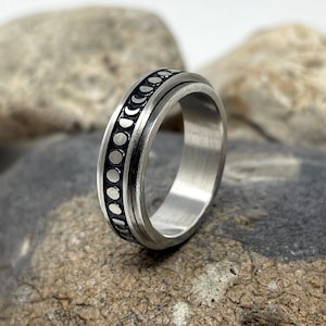 May include: A silver ring with a black band and a pattern of small circles around the band.