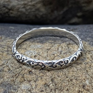 Peut inclure: Une bague en argent avec un délicat motif floral complexe. La bague est fine et a une finition polie.