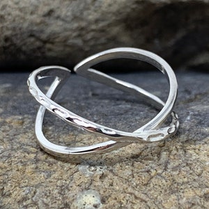 May include: A silver ring with a criss-cross design. The ring is made of two bands that are intertwined.