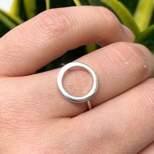 Puede incluir: Un anillo de plata con un diseño de círculo abierto grande. El anillo se lleva en un dedo.
