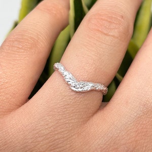 Puede incluir: Un anillo de plata con un diseño ondulado texturizado. El anillo se lleva en un dedo.