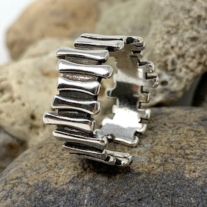 Puede incluir: Un anillo de plata con un diseño único que presenta una serie de barras verticales. El anillo está hecho de metal y tiene un acabado liso y pulido.