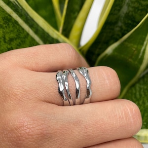 May include: A silver ring with a wavy, organic design. The ring is made of multiple bands that are stacked on top of each other.
