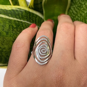 May include: A silver ring with a spiral design. The ring is on a finger and the background is a green plant.