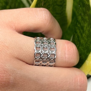 May include: A silver chain ring with multiple layers of interlocking links.