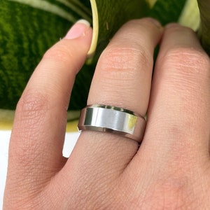May include: A silver band ring with a beveled edge.