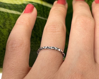 May include: A silver ring with a braided design. The ring is worn on a person's finger.