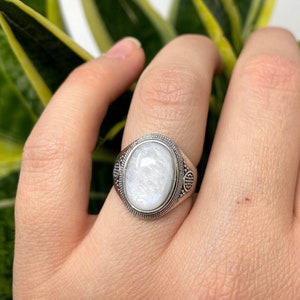 Peut inclure: Une bague en argent avec une pierre de lune ovale blanche sertie dans une bande décorative.