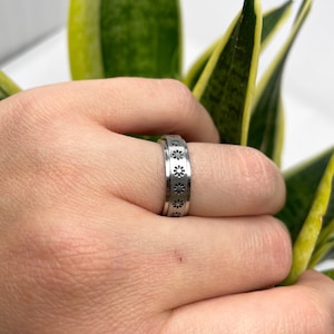 May include: A silver ring with a band of small, black flower designs.