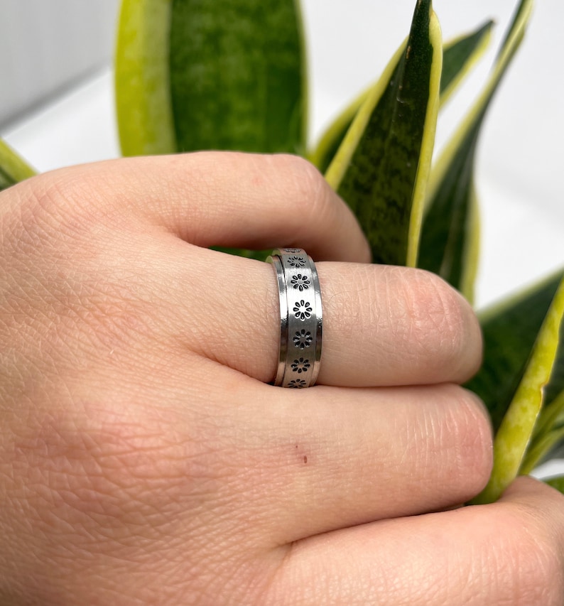 May include: A silver ring with a band of small, black flower designs.