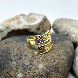 May include: A gold-toned ring with a delicate, intricate design. The ring is made of two bands that are intertwined and have a floral pattern.