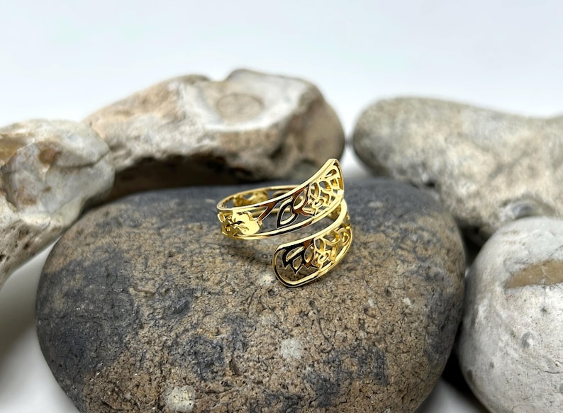 May include: A gold-toned ring with a delicate, intricate design. The ring is made of two bands that are intertwined and have a floral pattern.