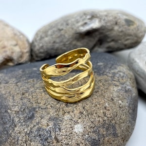 May include: Gold ring with a textured, wavy design. The ring is made of multiple bands that are intertwined.